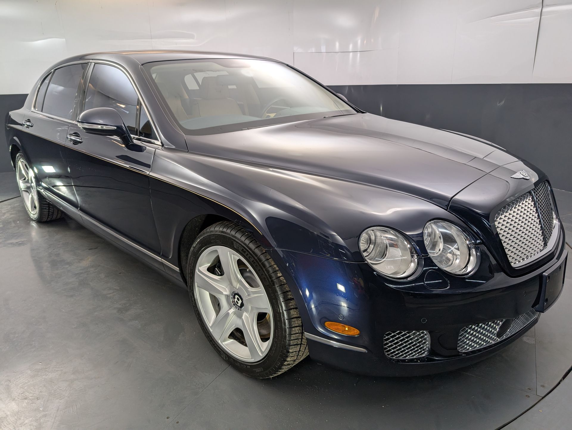 Dark blue luxury sedan parked indoors in a showroom, front three-quarter view