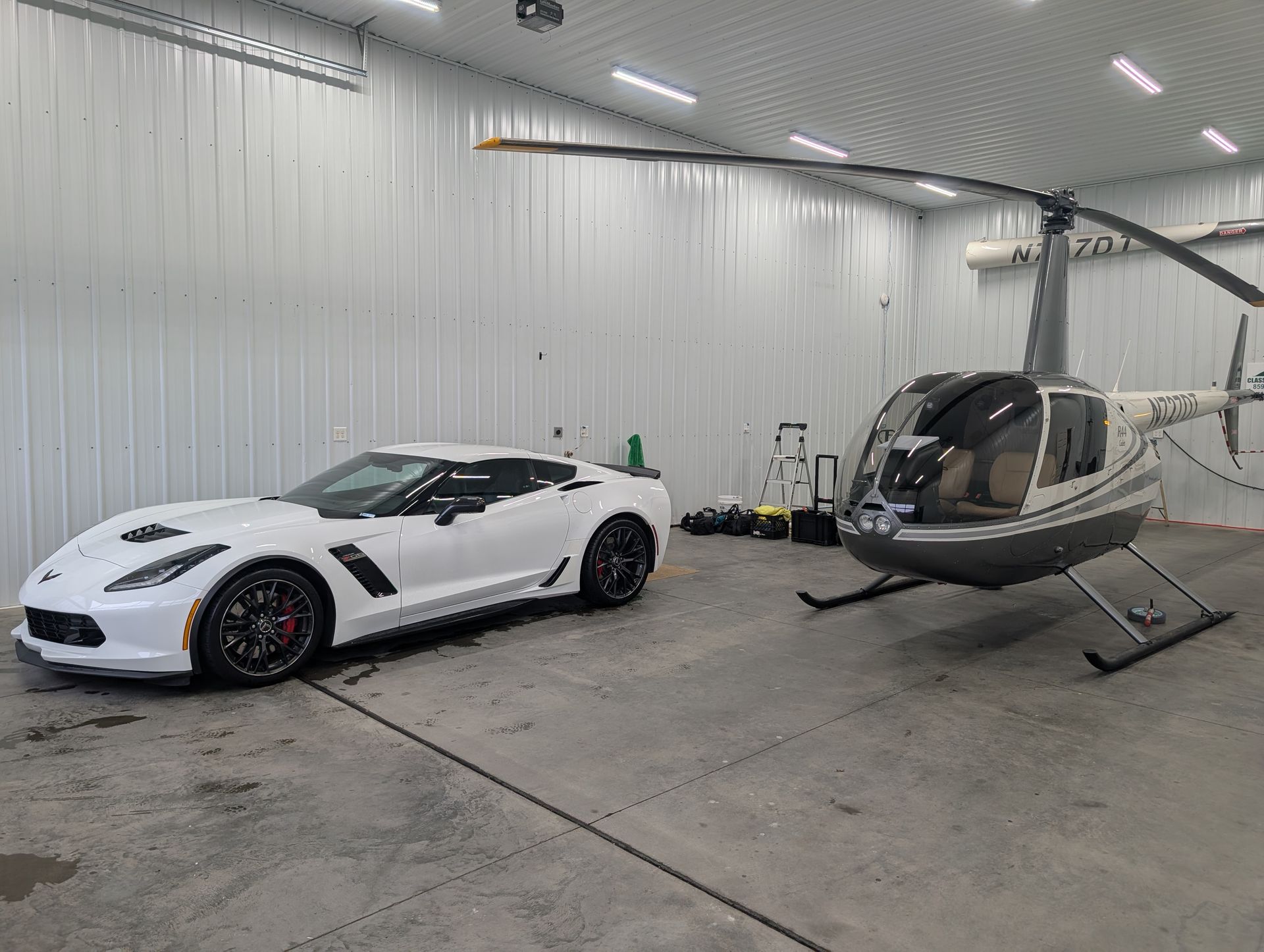 White sports car and gray helicopter parked inside a bright hangar.