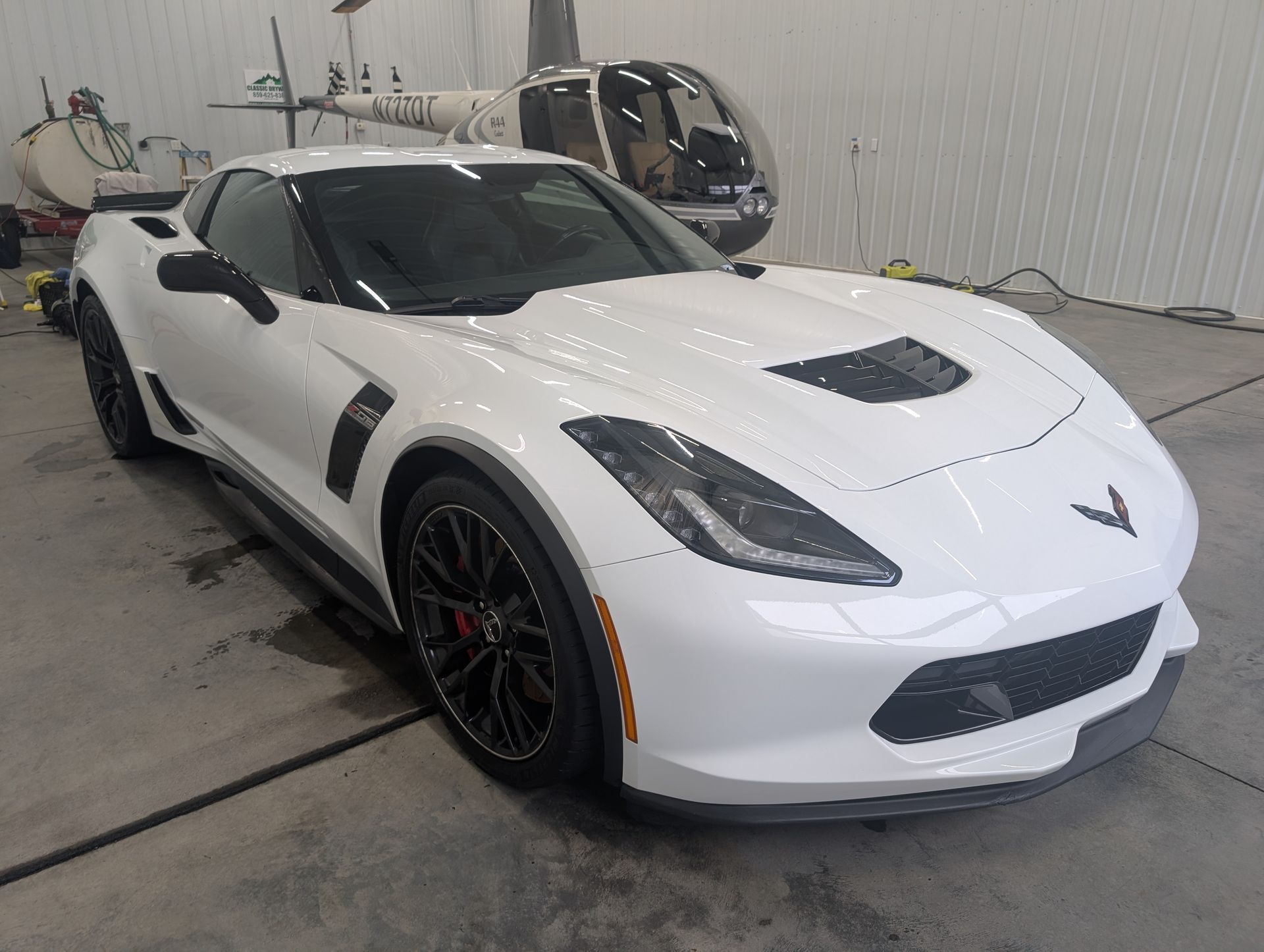 White Chevrolet Corvette in a garage, front-left view, with black trim and wheels.