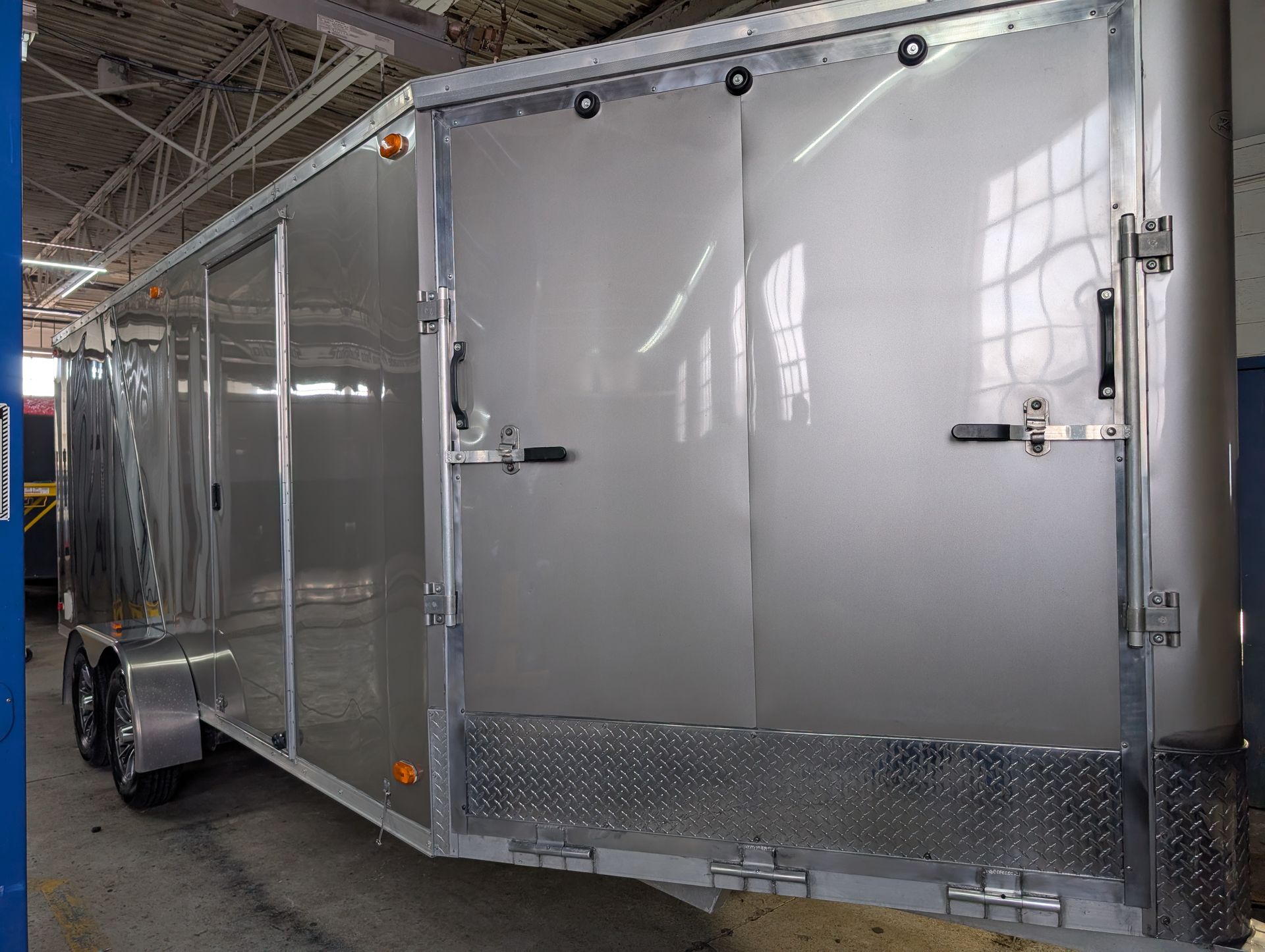 Silver enclosed cargo trailer with rear double doors inside a warehouse