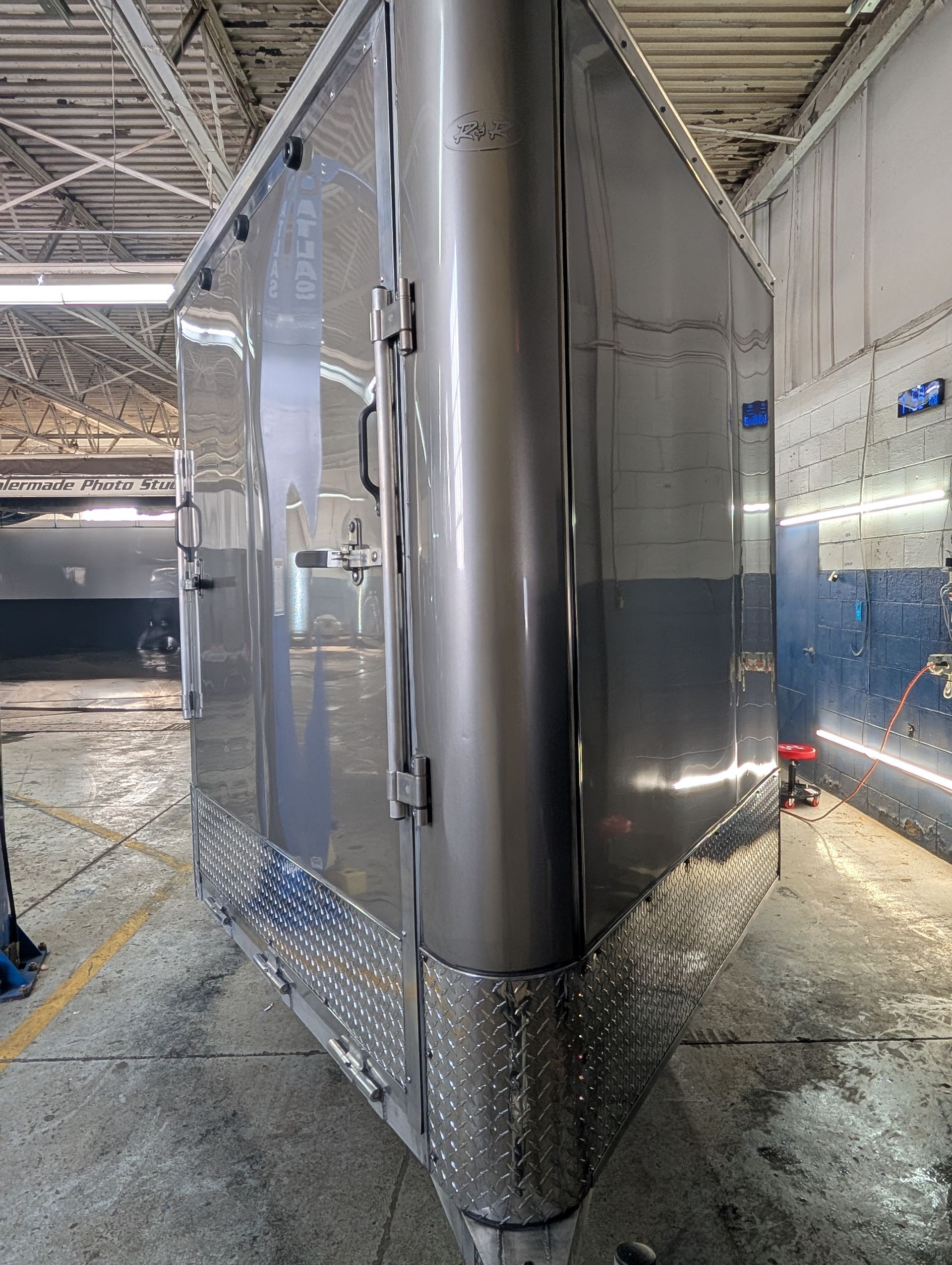 Shiny stainless steel trailer inside a warehouse, with a diamond-plate lower edge and wet floor.