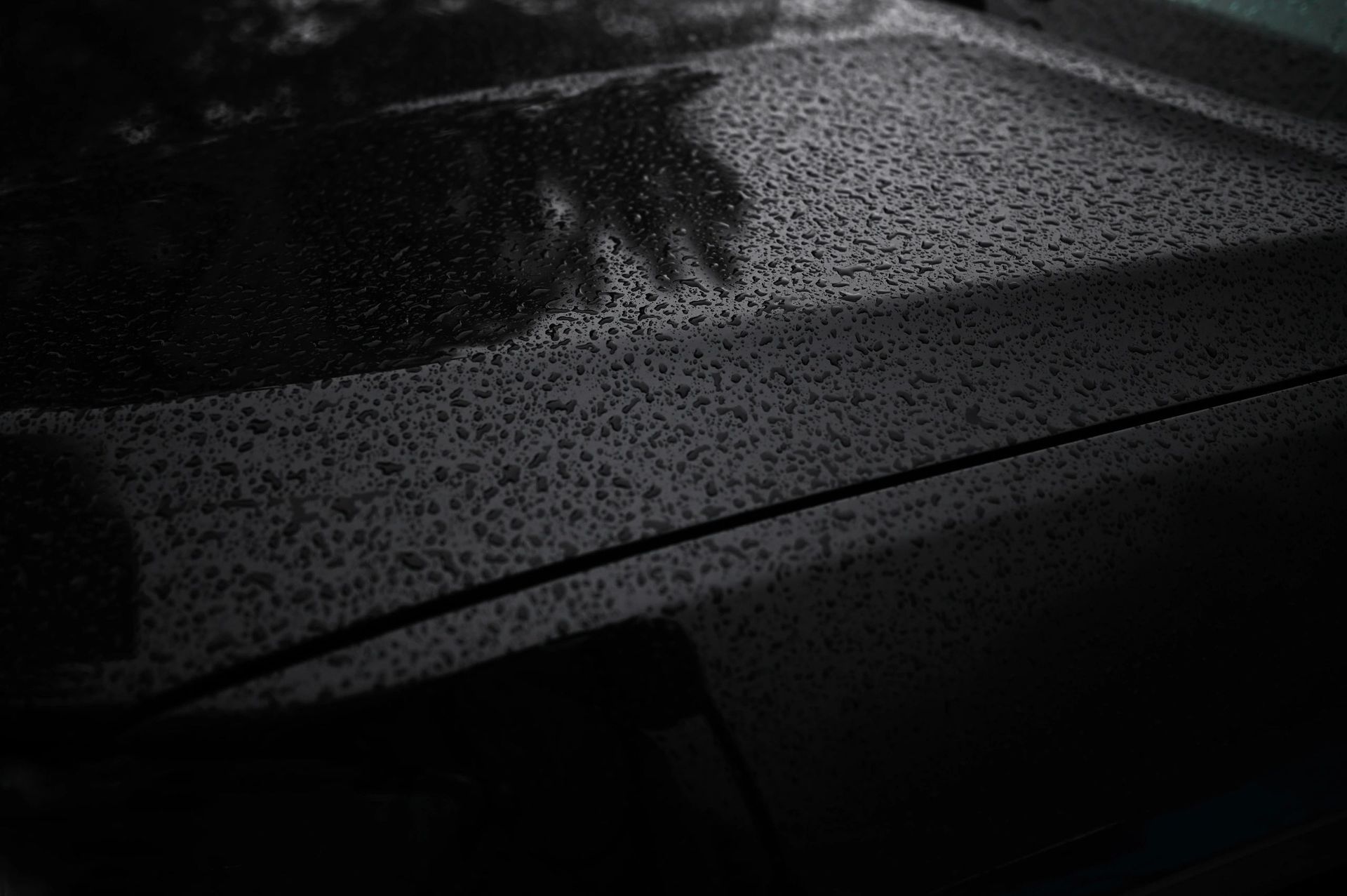 Rain-speckled car hood and windshield in a dark, wet setting