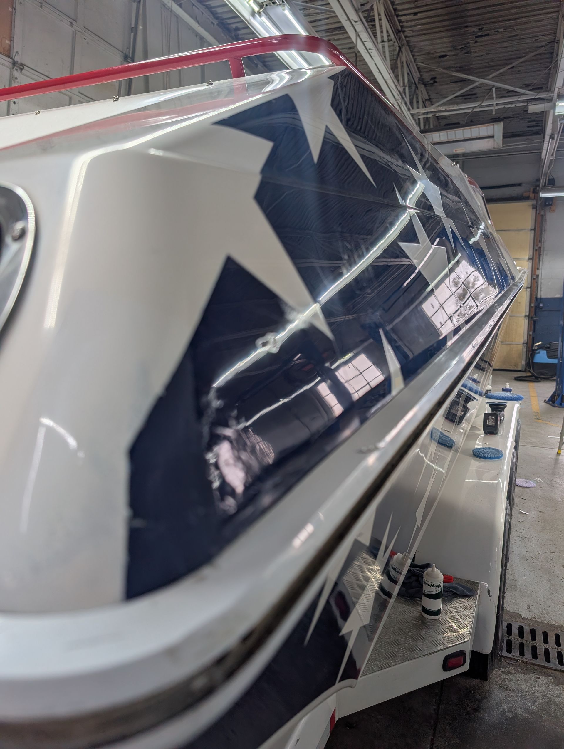 Close-up of a white and navy boat hull being polished in a workshop.