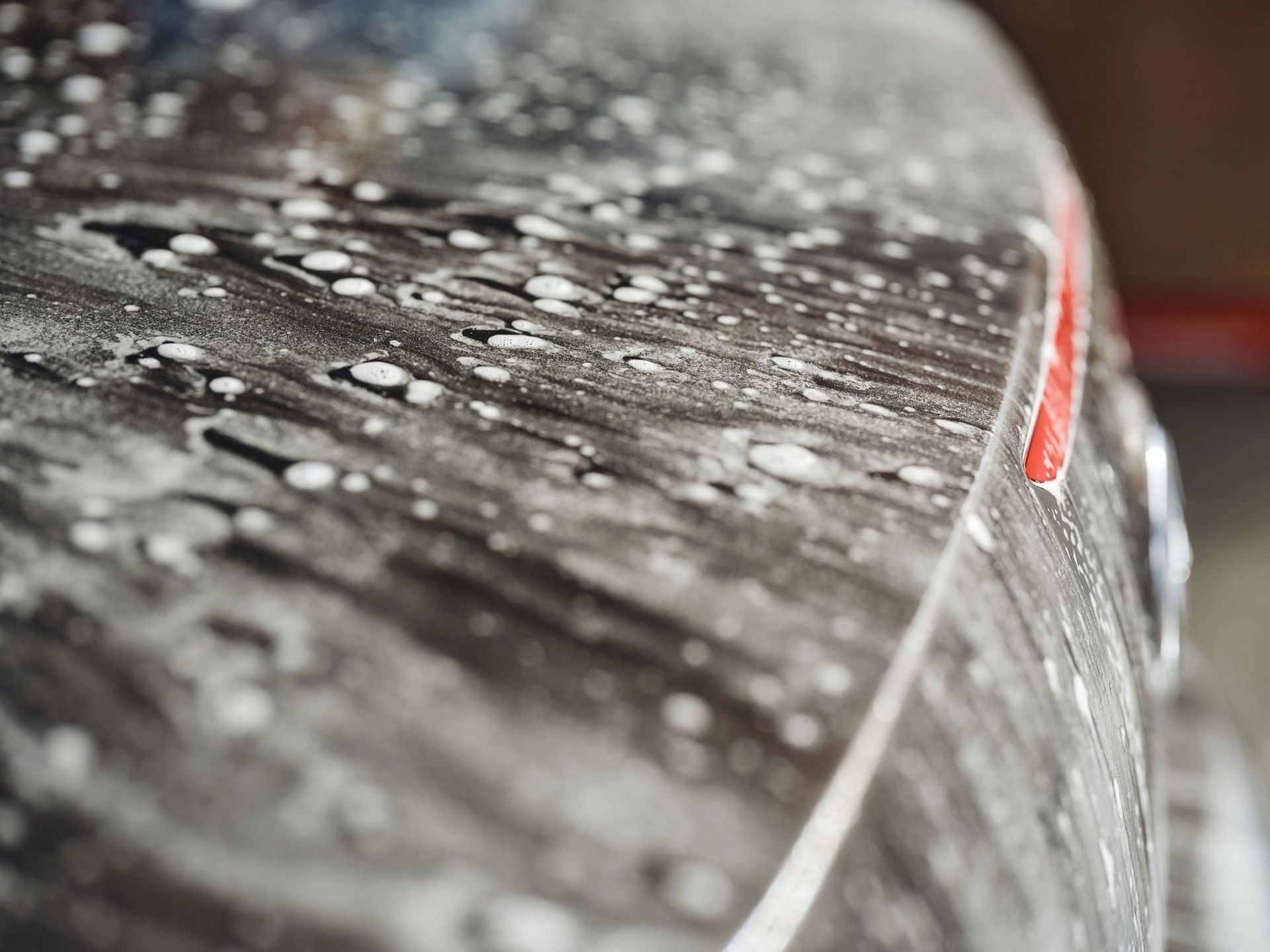 Close-up of a wet, snow-covered car hood with water droplets and a red taillight edge