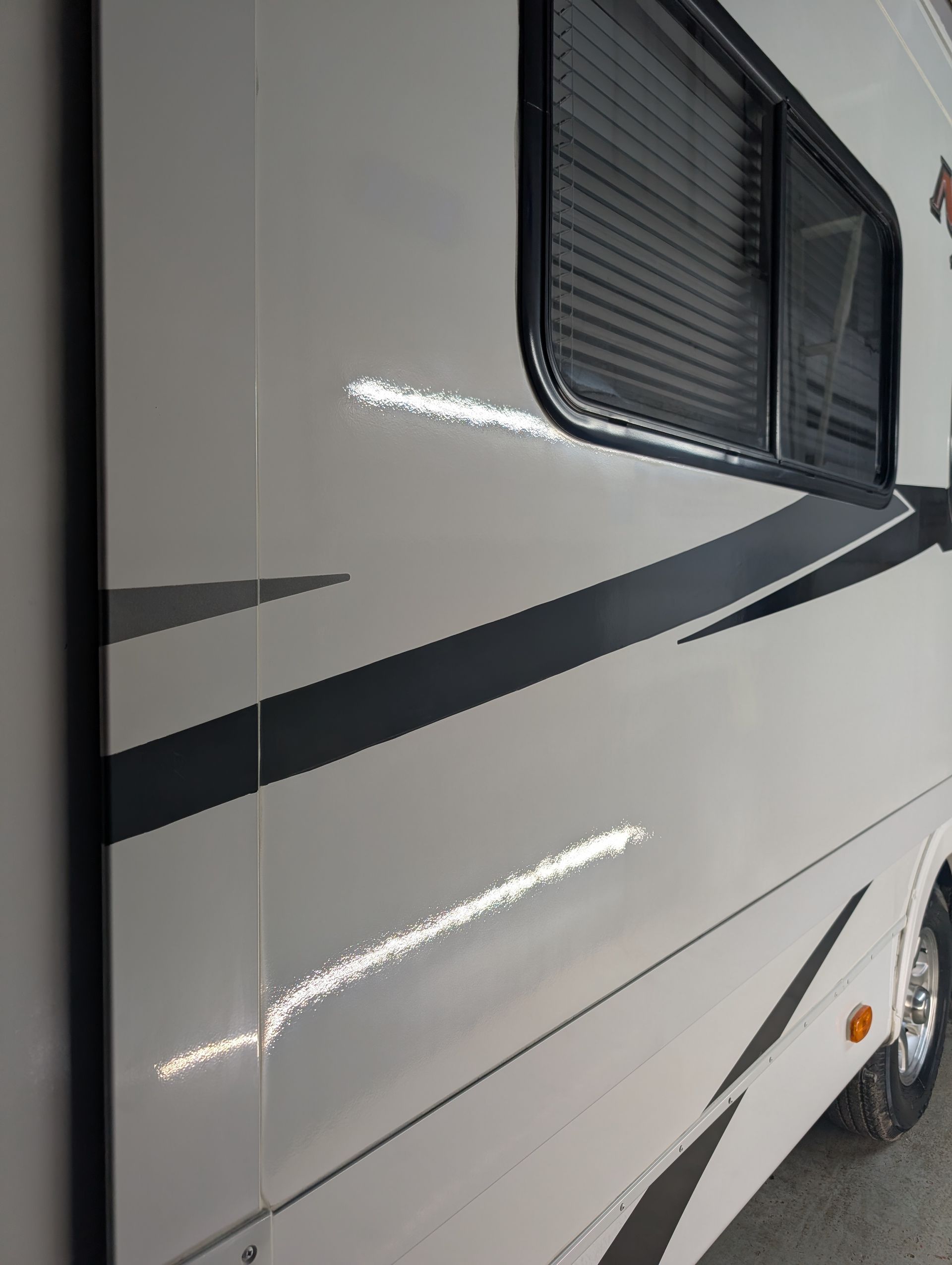Close-up of a white RV side with black stripe and tinted window