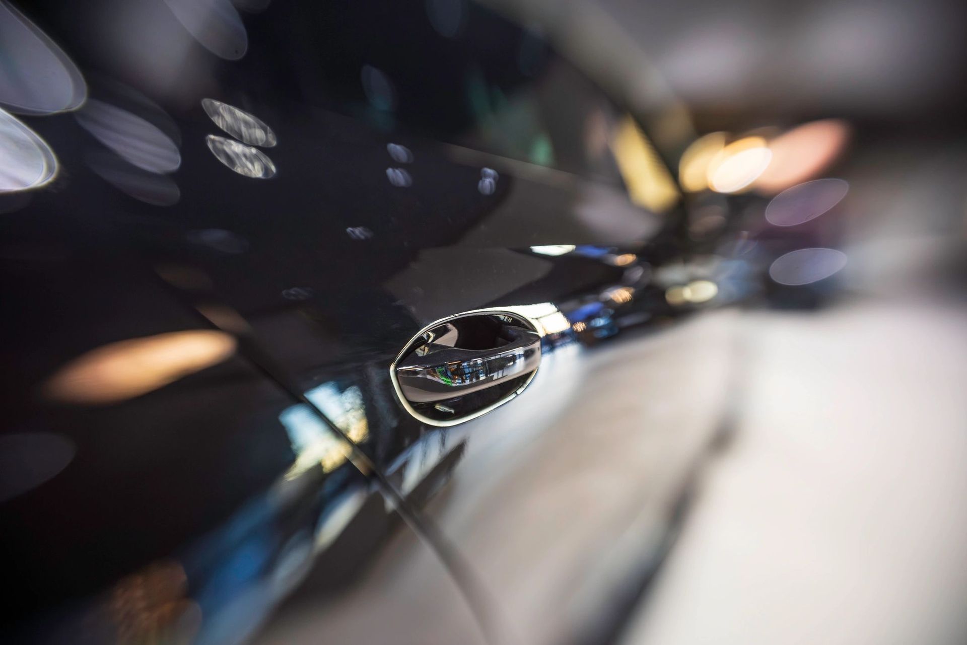 Close-up of a car side mirror reflecting blurred lights on a glossy black vehicle