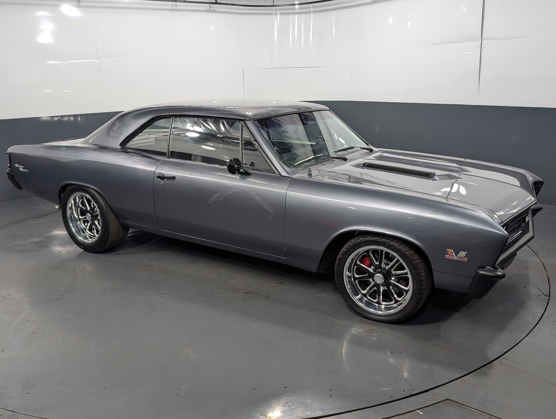 Gray classic muscle car parked in a white studio, front three-quarter view.