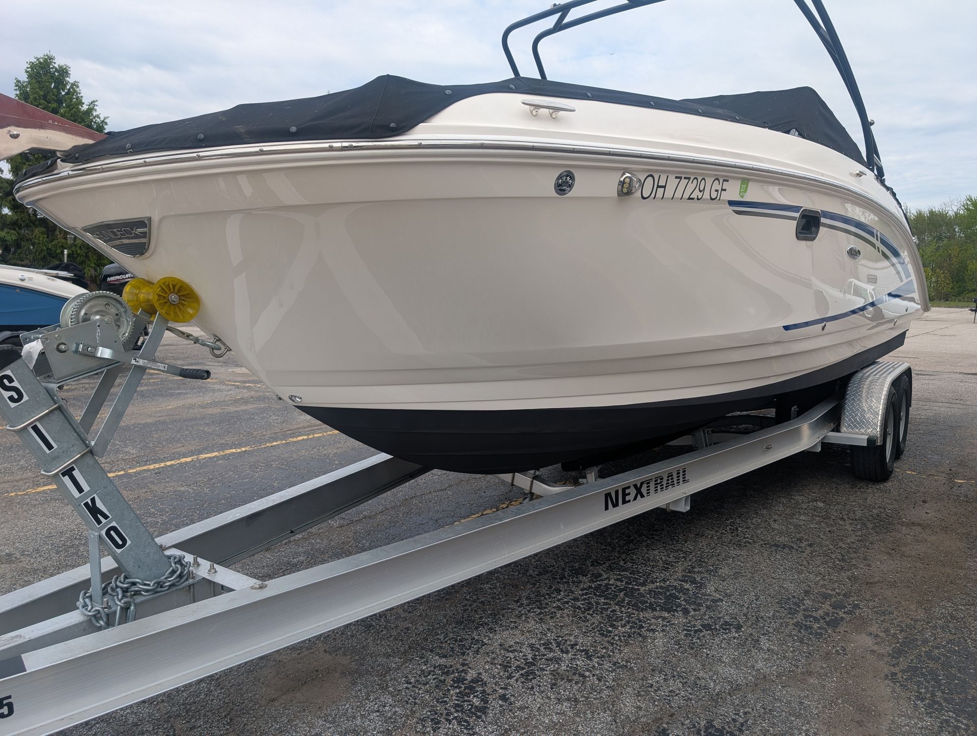 White motorboat on a trailer at a gravel lot, viewed from the front-left side.