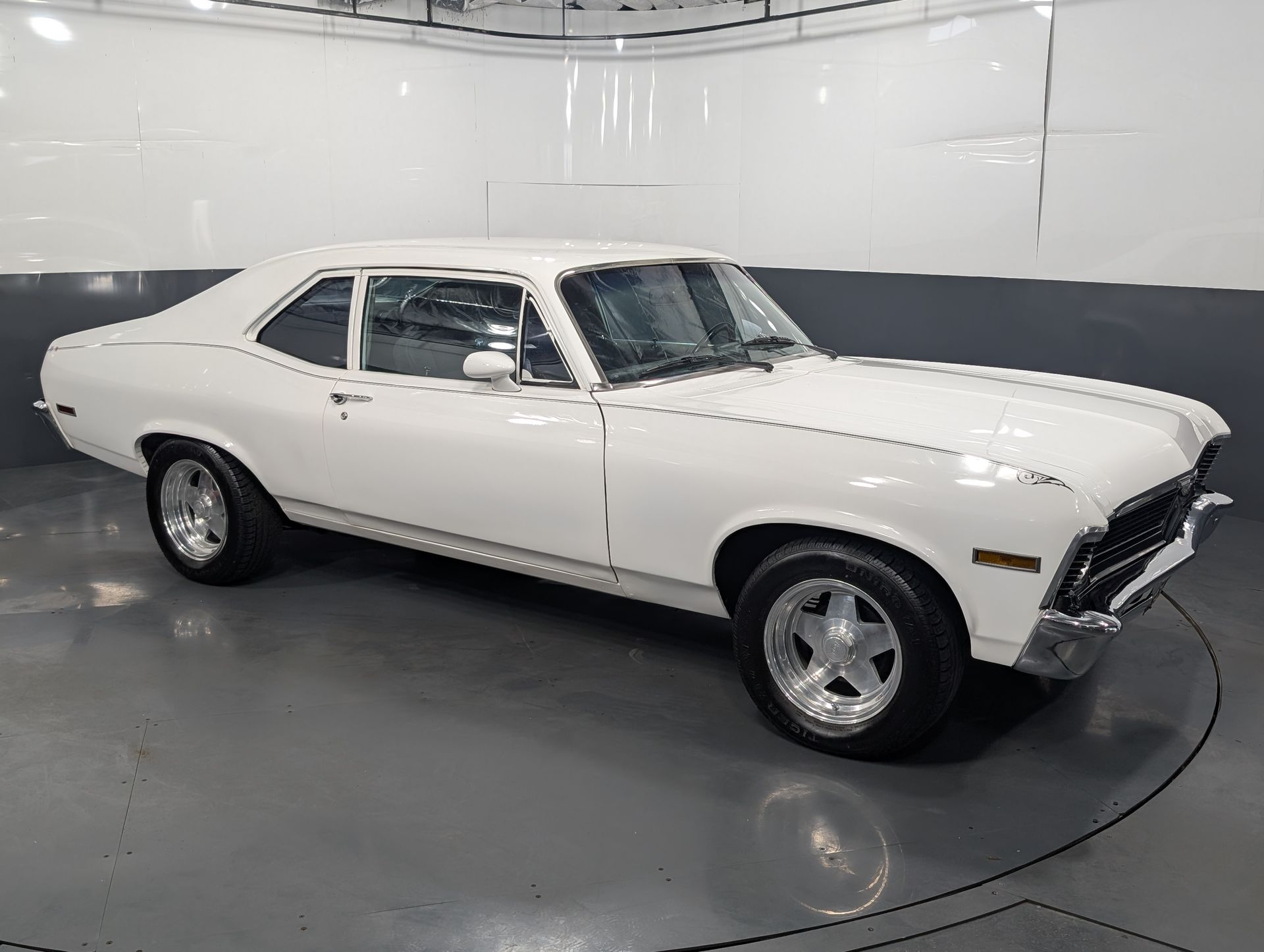 White classic muscle car parked in a showroom, viewed from the side.