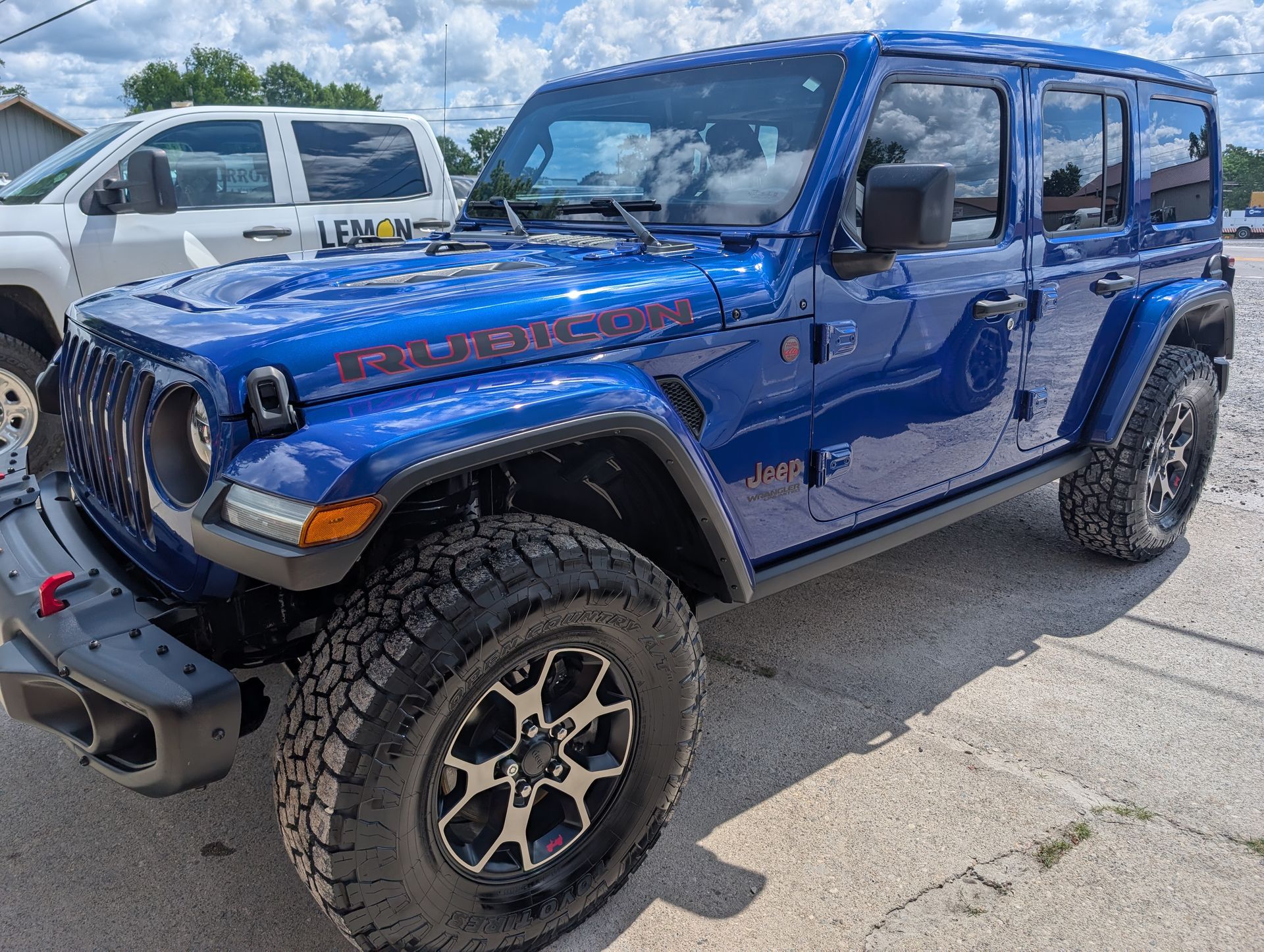 Blue lifted Jeep Wrangler parked in a lot, with off-road tires and black trim.