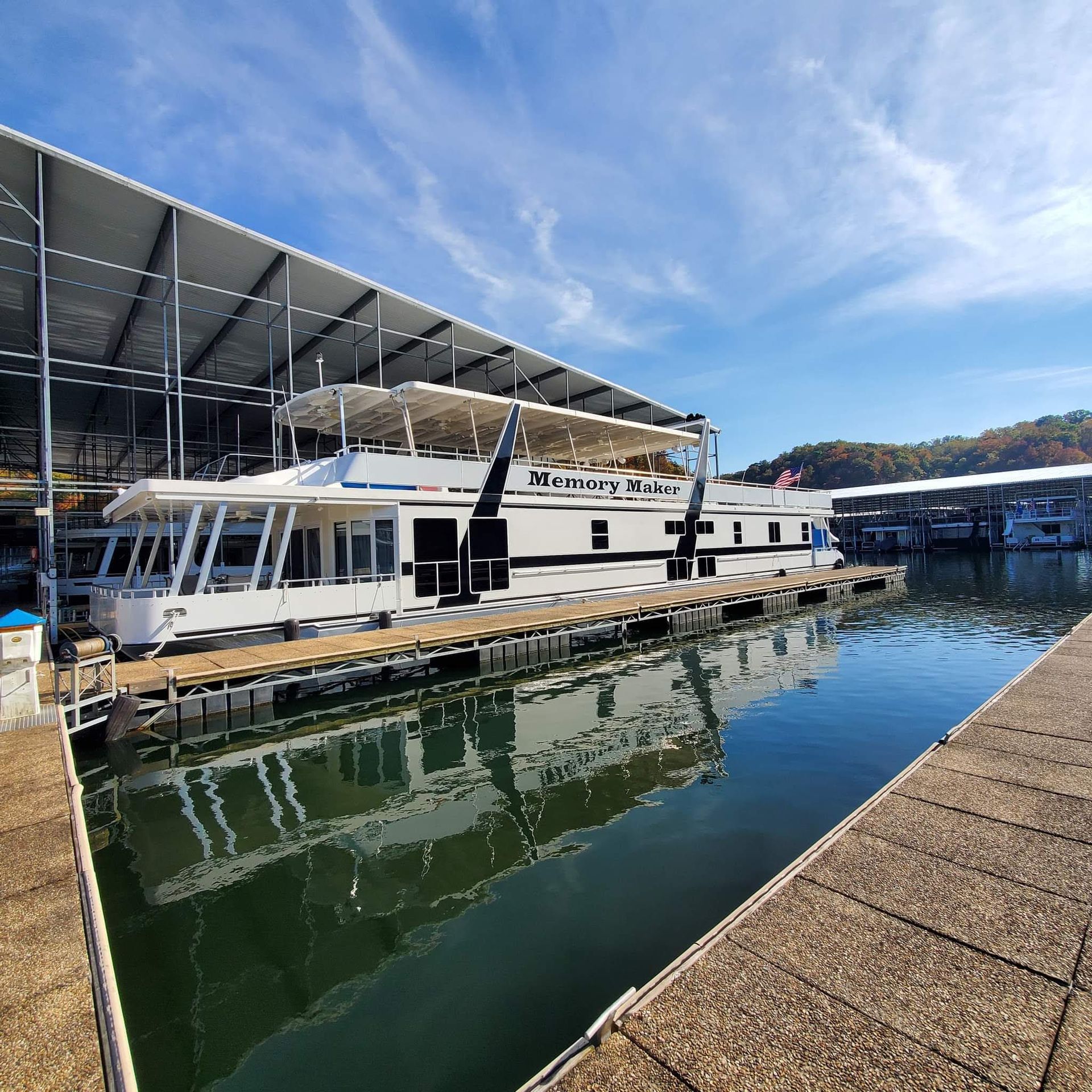 White passenger boat docked in a marina beside a covered pier, with calm water reflecting the scene.