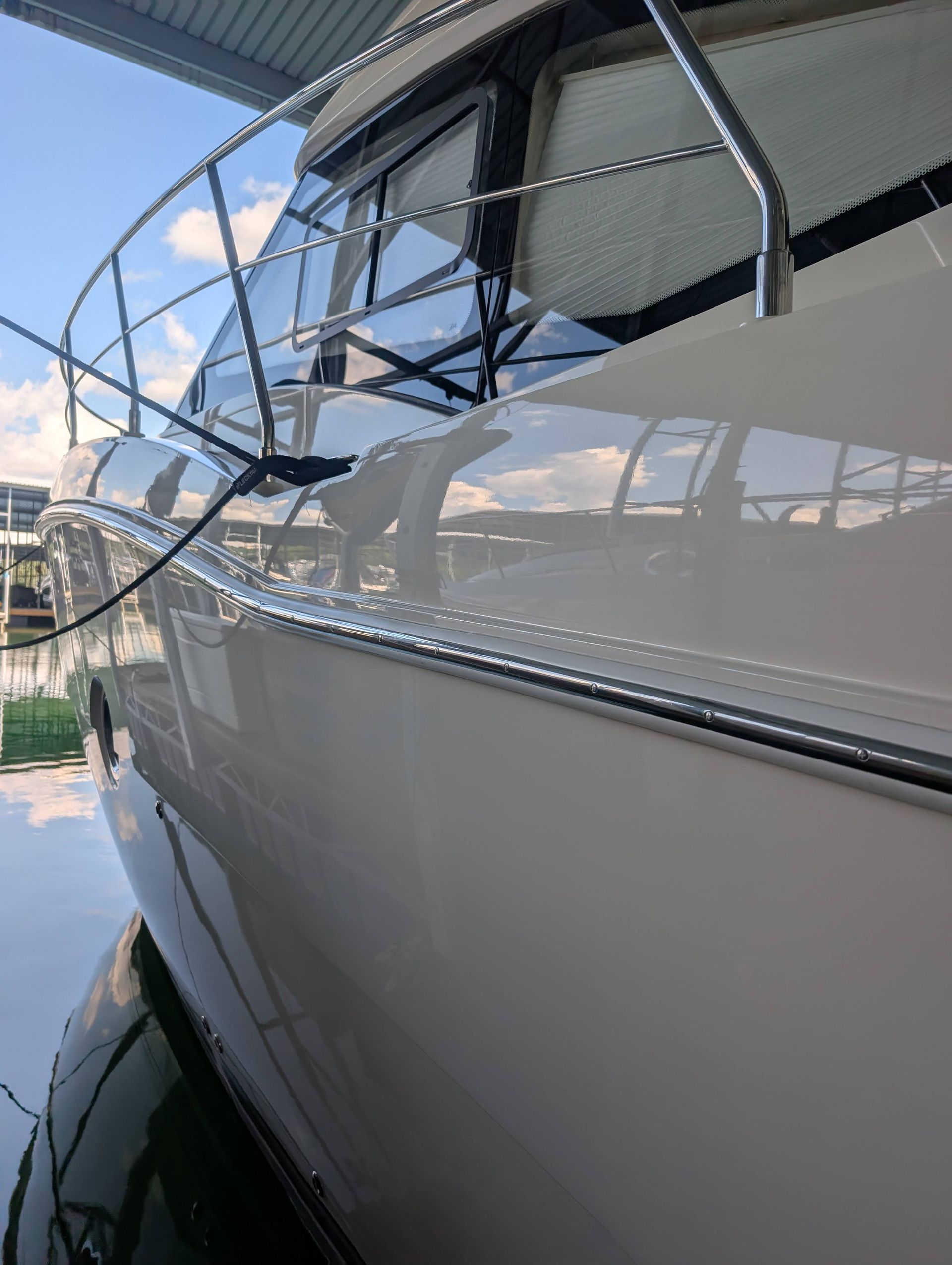 White boat hull with dark-tinted windows docked by the water under a canopy