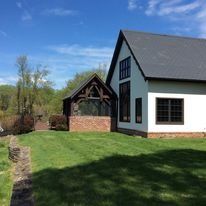 White house with dark trim and gray roof next to a brick and wood structure on a sunny day.