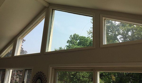 Three triangular windows above rectangular windows, showing a blue sky and trees outdoors.