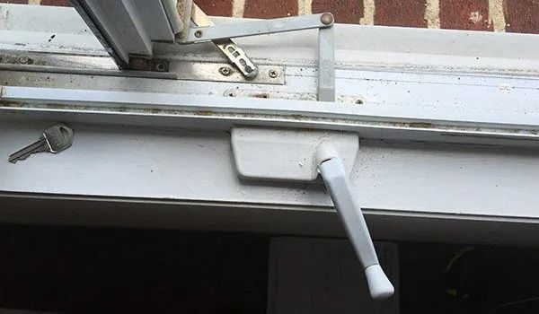 White window with a crank, key, and hinges against a brick wall.