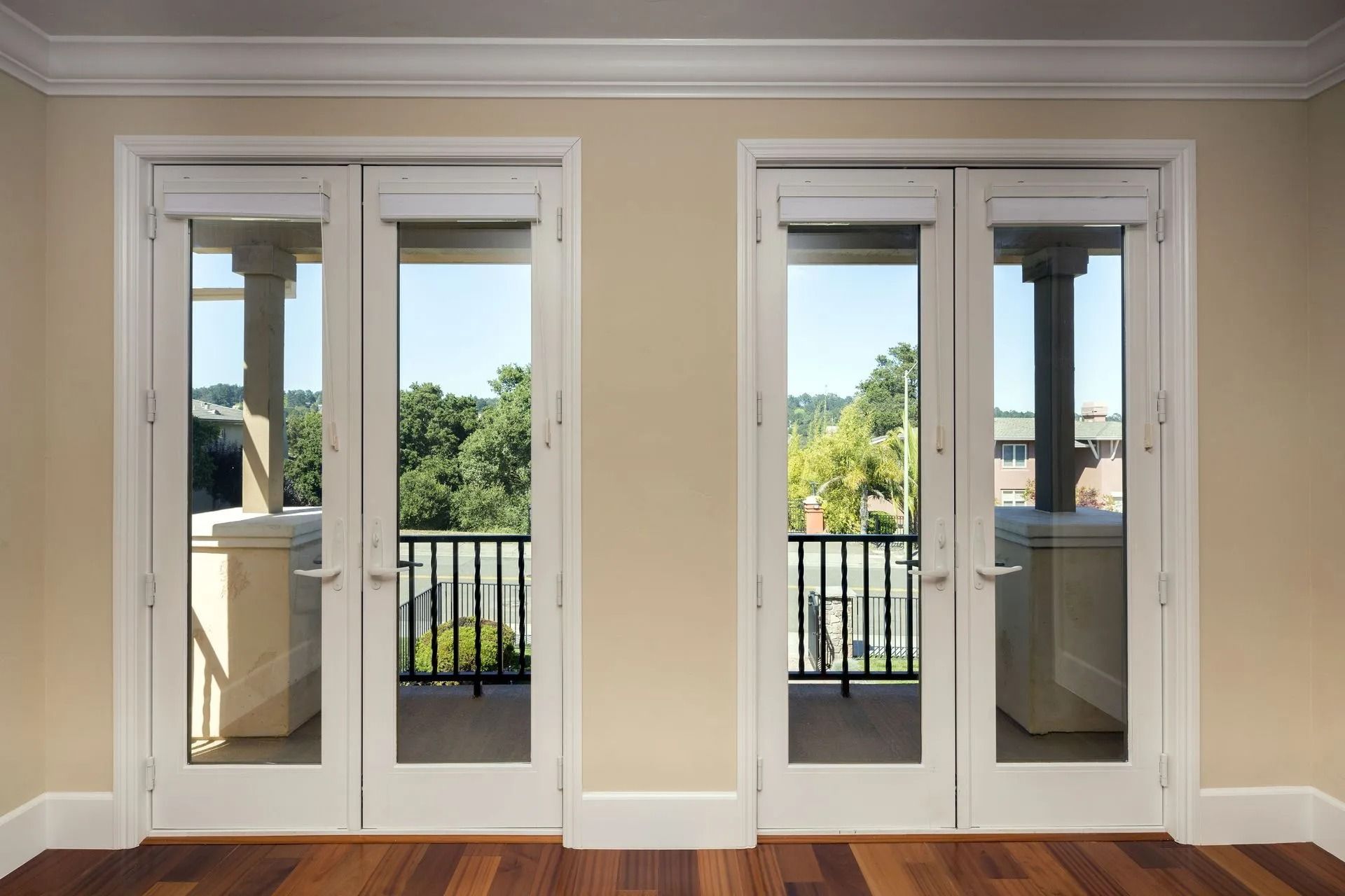 Two white French doors with glass panels, opening onto a balcony with green trees and black railings.