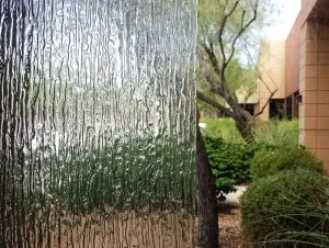 Textured glass panel reflecting greenery and a building, outdoors.