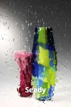 Two colorful glass vases, one red, one blue and green, behind a wet window.