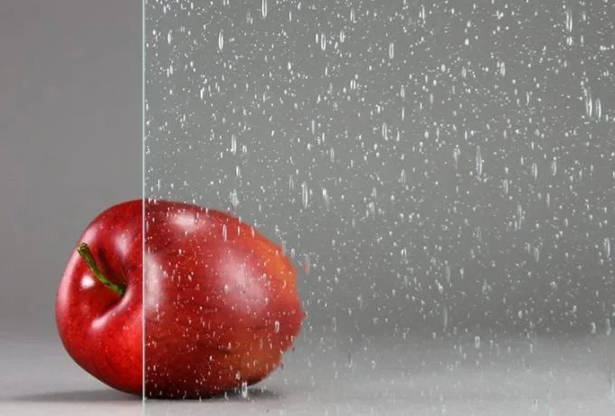 Red apple partially obscured by clear glass with a rain-like pattern on a gray background.