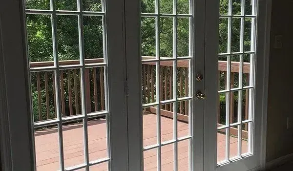 White French doors with multiple panes open onto a wooden deck overlooking green trees.