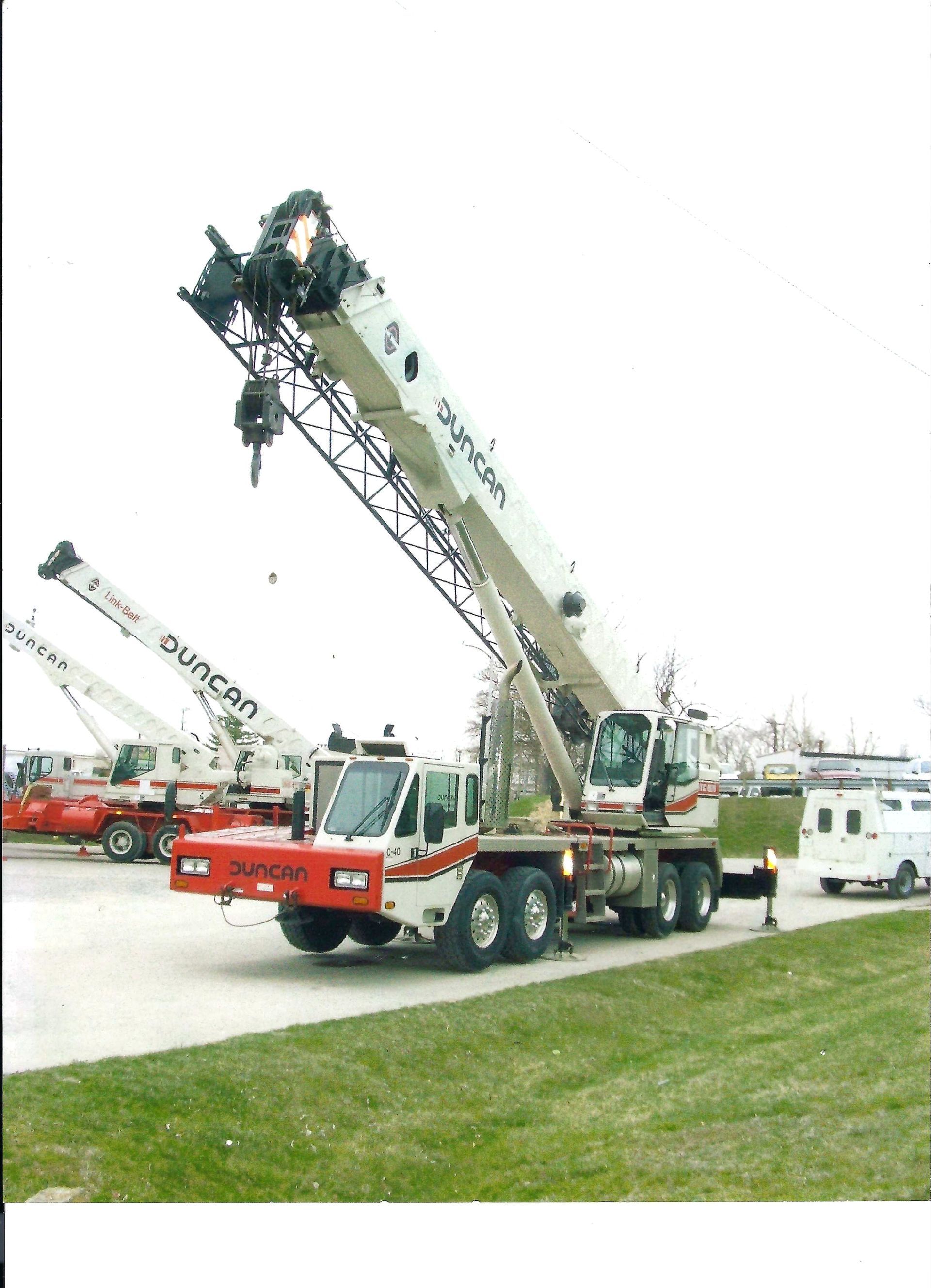 Line of large crane trucks parked on grass, red and white one with boom raised in front