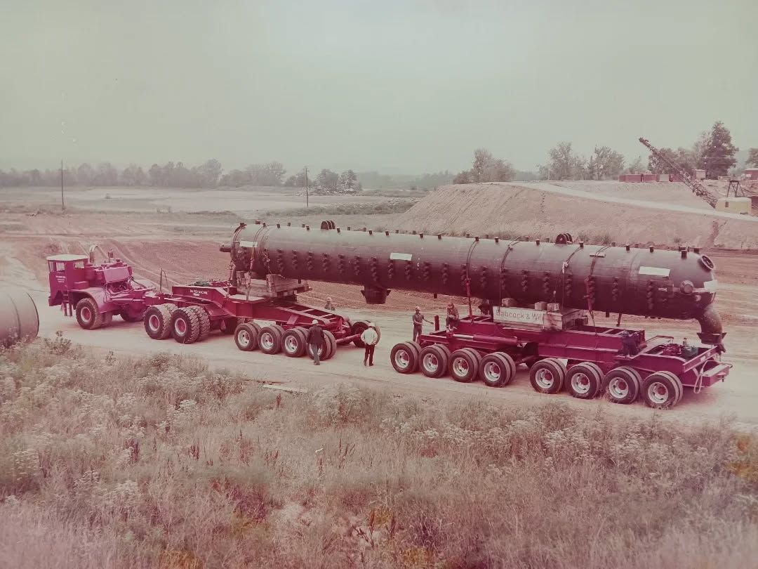 Red trucks pulling a long cylindrical tank trailer along a snowy field road