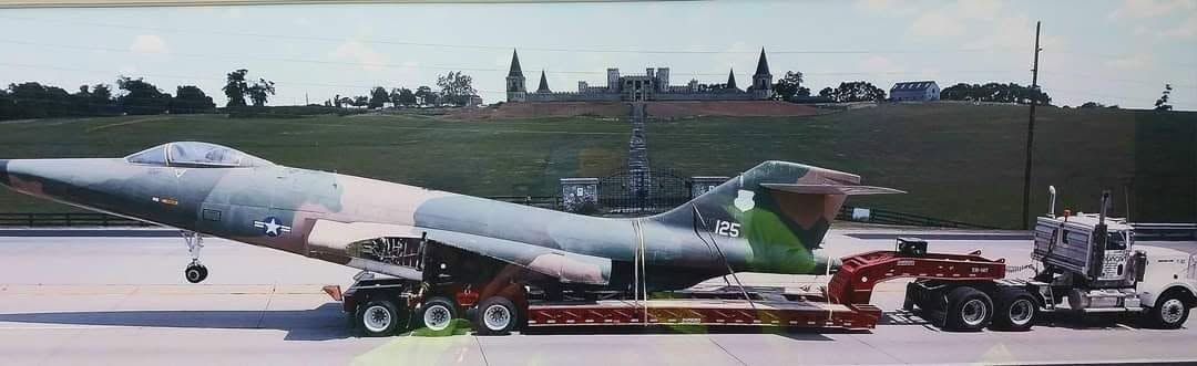 Military jet being towed on a runway by a red tractor, with support vehicles nearby