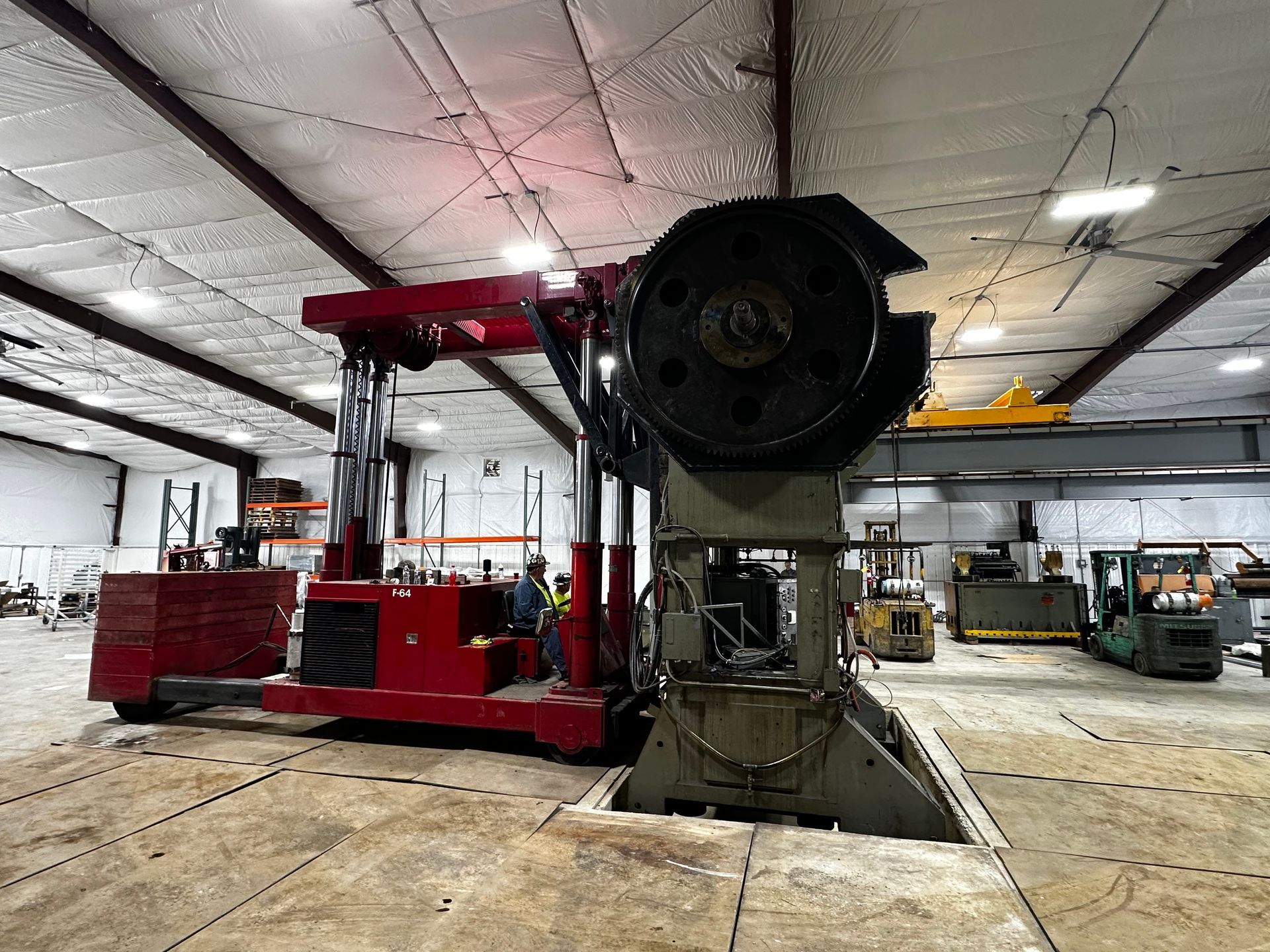 Large red industrial machine in a warehouse, with a black circular component in front and a ceiling crane above