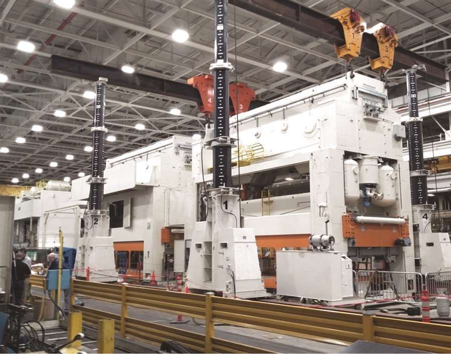 Large white industrial press machine on a factory floor, with overhead crane and safety railings