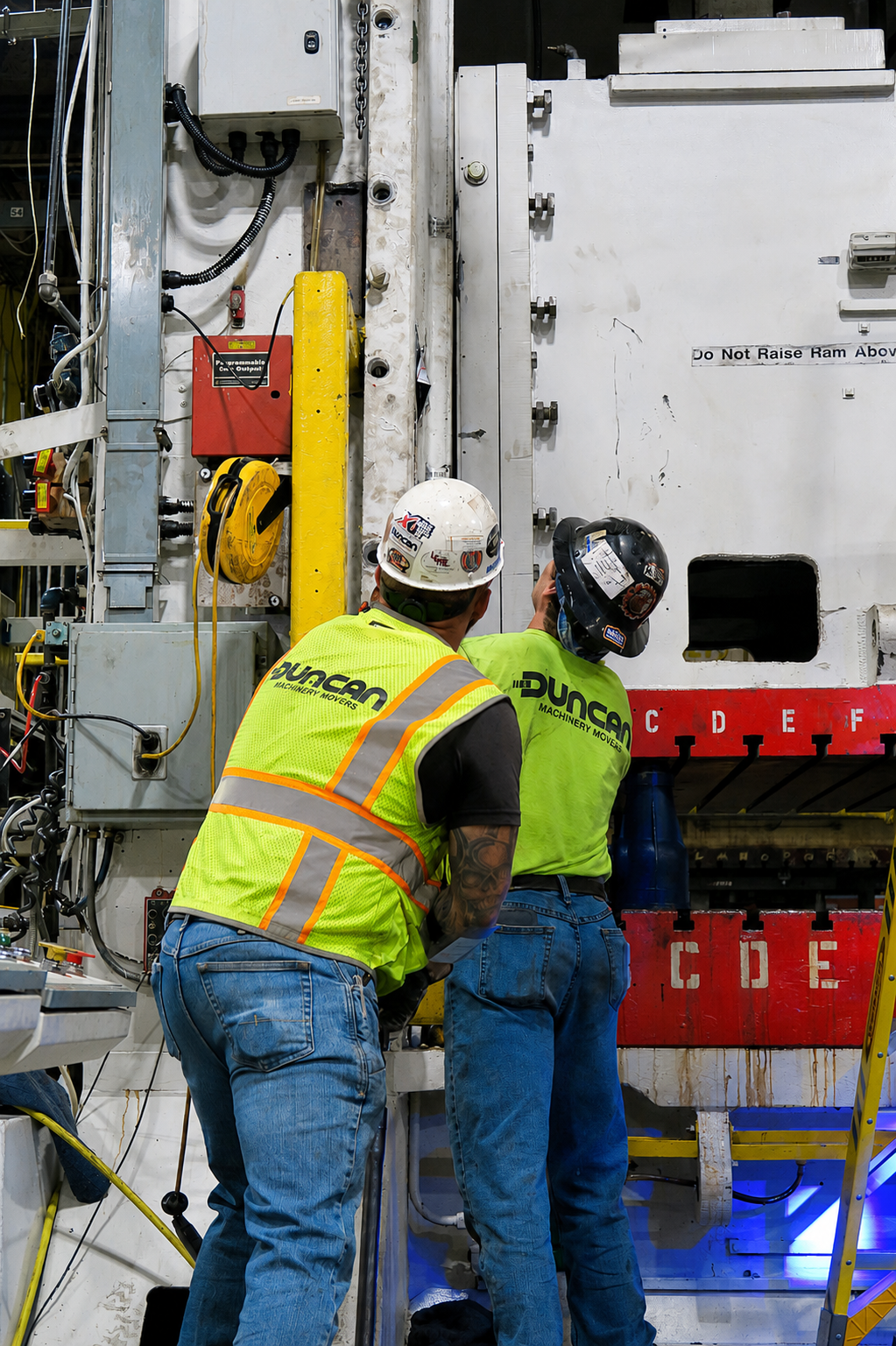 Two workers in safety vests inspect a large industrial machine in a factory