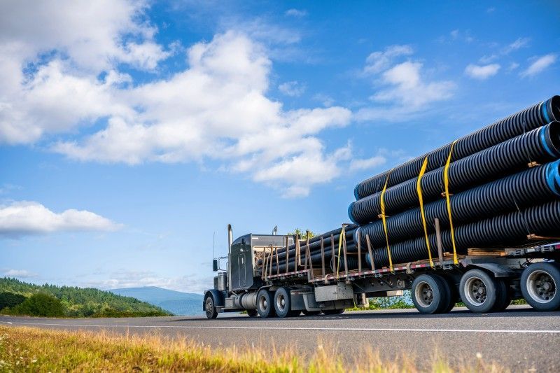 A semi truck is carrying a load of pipes down a highway.