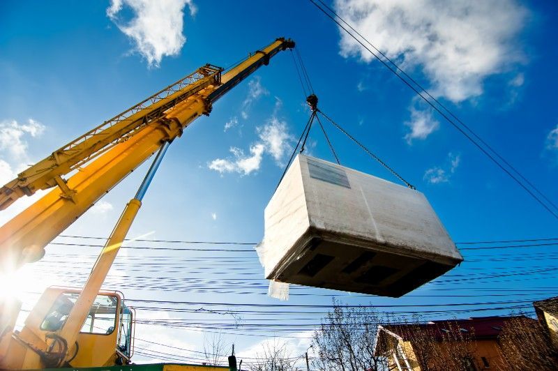 A crane is lifting a large concrete box into the air.