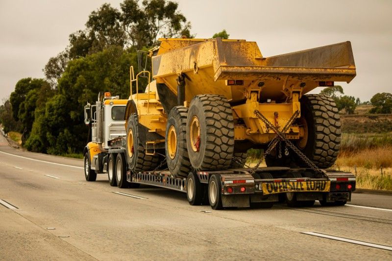 A semi truck is carrying a large yellow dump truck on a trailer.