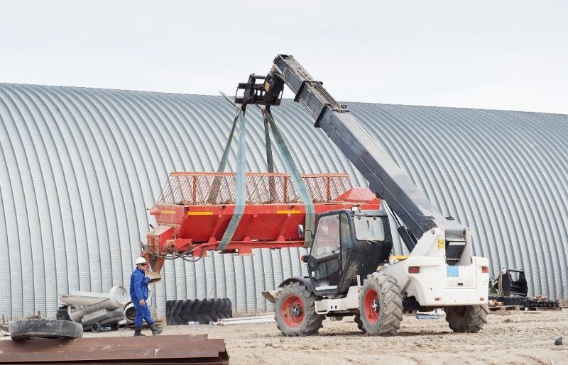 A man is standing next to a tractor that is lifting a large object.