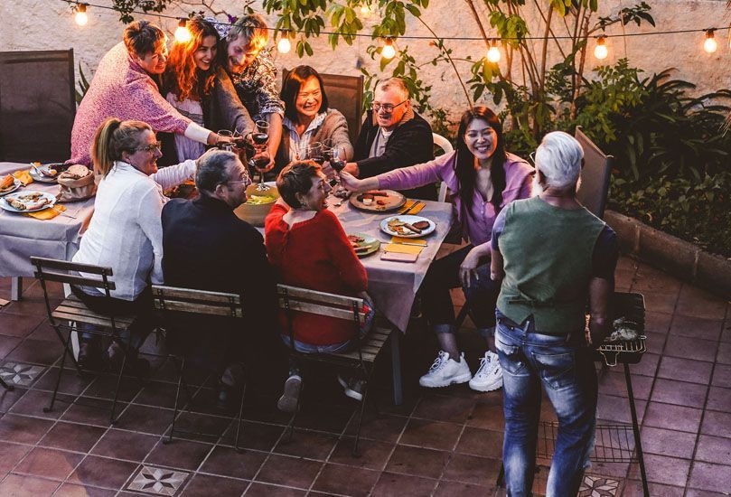 People toasting at an outdoor dinner party with string lights above a table of food.
