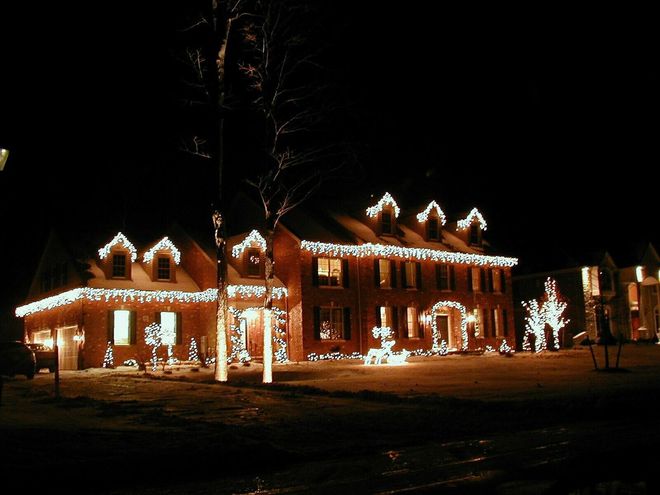 Large brick house at night, lit up with Christmas lights, snow on roof.