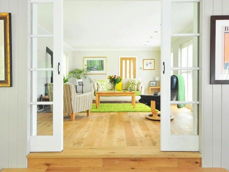 Bright living room with open French doors, wooden floor, and yellow sofa near a green plant.