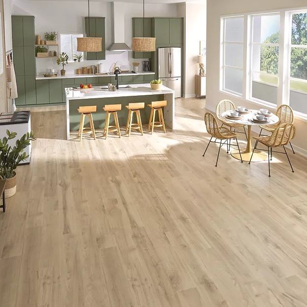 Bright modern kitchen with sage cabinets, island stools, and a sunlit dining nook by large windows.