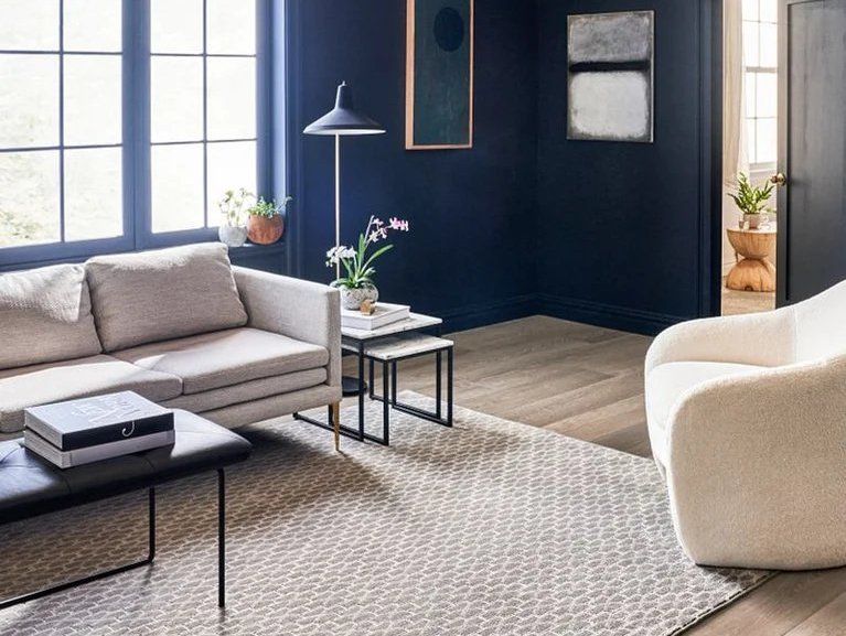 Modern living room with gray sofa, black coffee table, cream chair, and dark blue accent wall