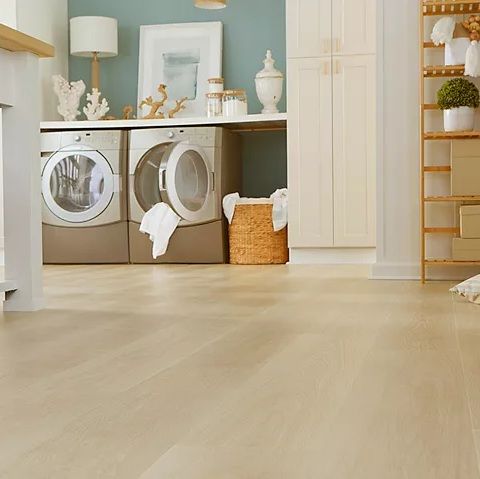 Bright laundry room with front-loading washer and dryer, light wood floor, and white cabinetry on a pale blue wall