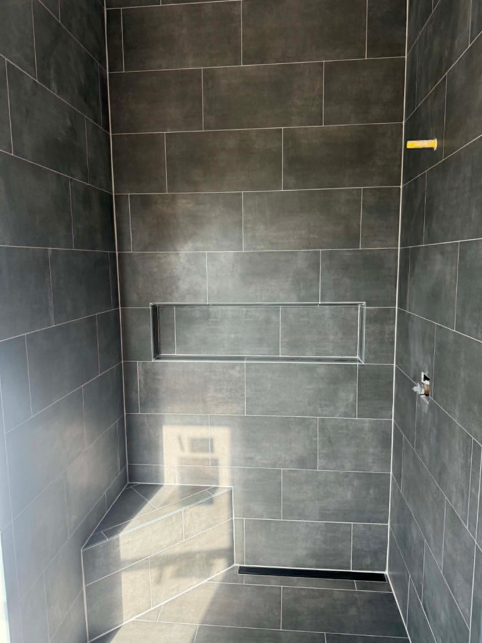 Empty black-tiled shower stall with a built-in bench and sunlight on the floor