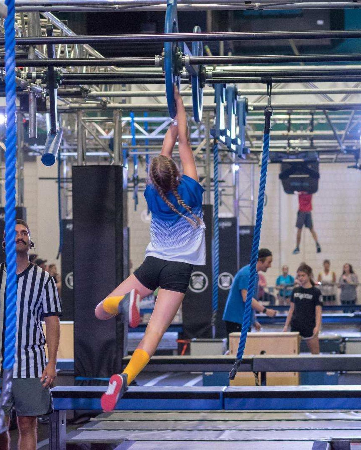 A woman is jumping over a bar in a gym.