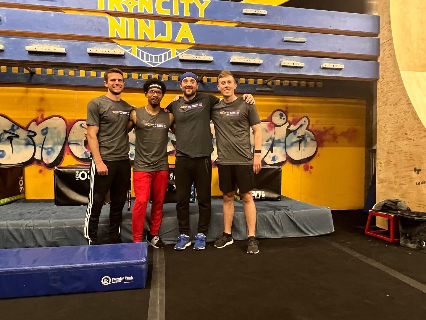 A group of men are posing for a picture in front of a sign that says ninja.