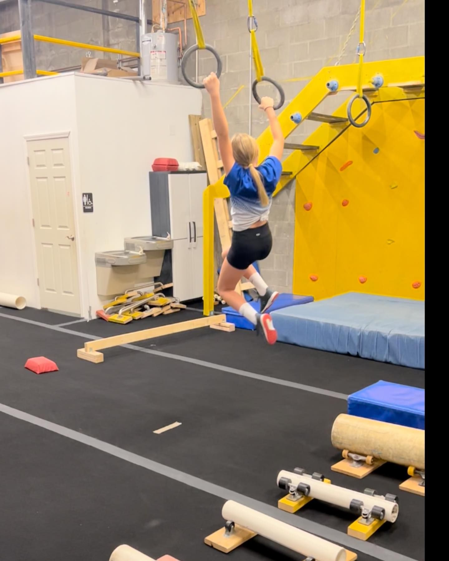 A girl is jumping over a balance beam in a gym