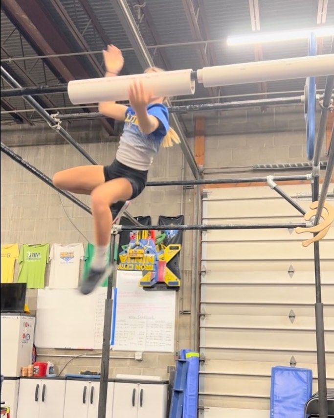 A young girl is doing a handstand on a bar in a gym.