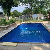 A large swimming pool surrounded by trees and houses in a backyard.