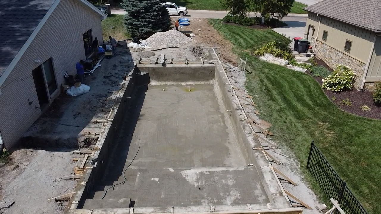 Concrete driveway under construction beside a house, with dirt, forms, and landscaping along the edges.