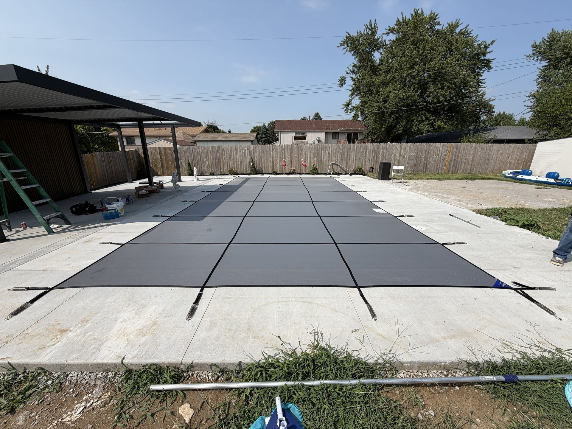 Backyard with a large gray mat or platform on a concrete area, near a covered patio and fence