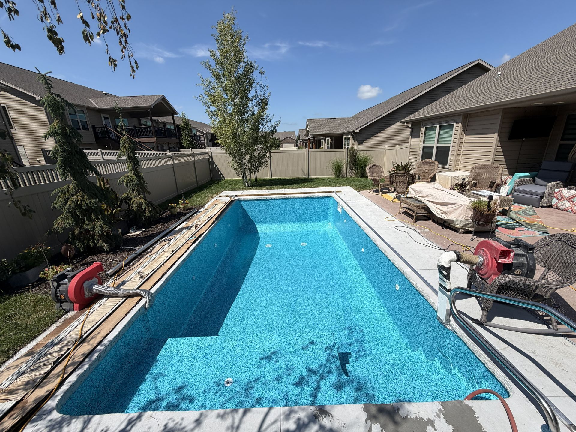 Backyard swimming pool with blue water, patio furniture, and a covered grill on a sunny day