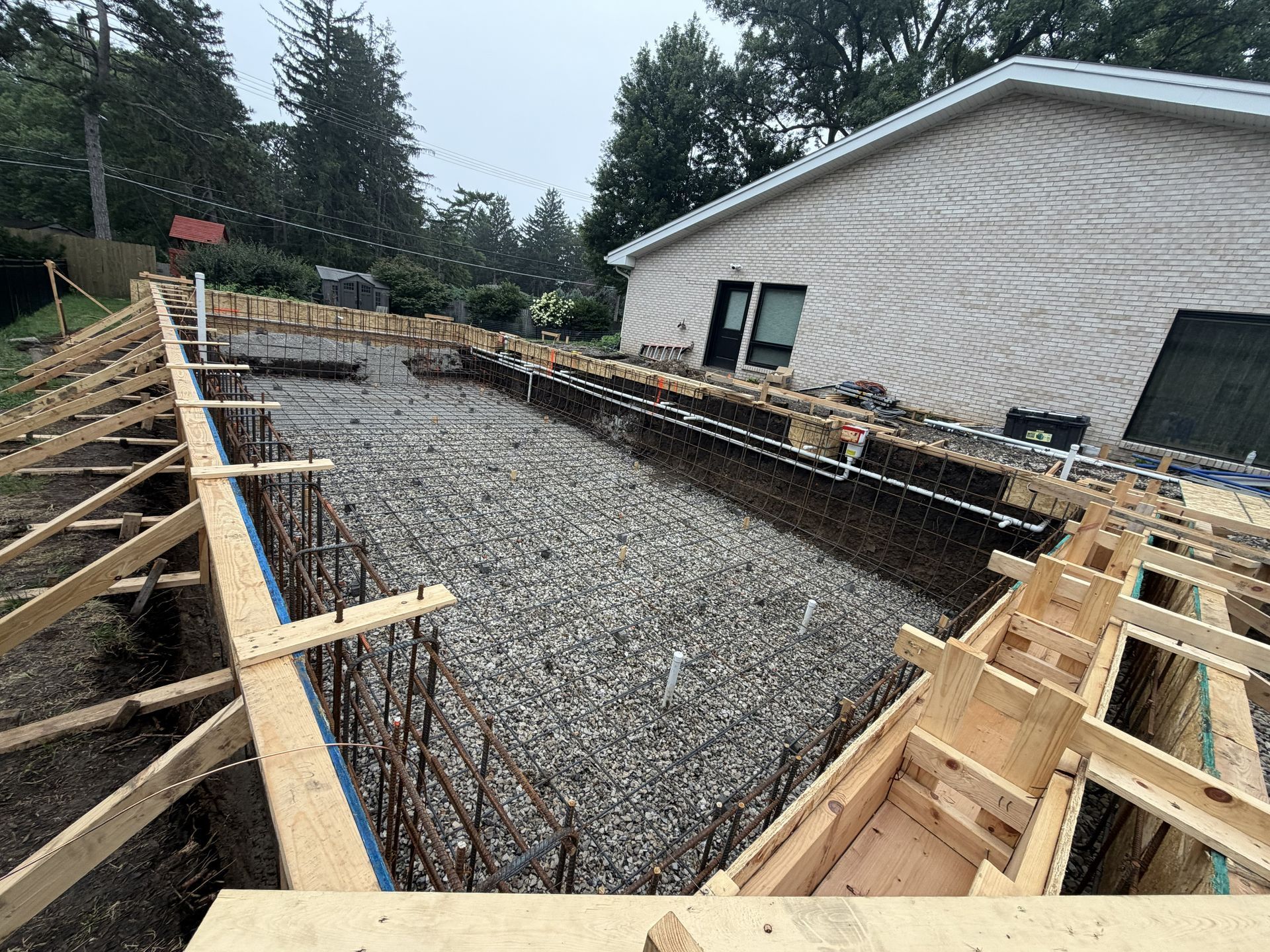 Foundation under construction with wooden forms and gravel beside a house